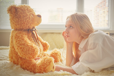happy girl lying with teddy bear in sun light, toned imageの写真素材