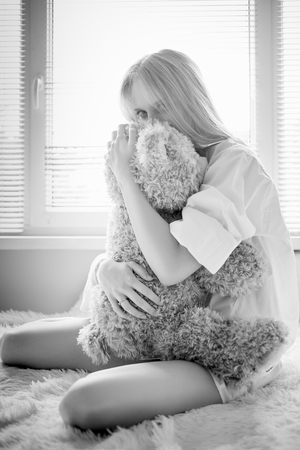 sensual girl sitting with teddy bear in sun light, monochrome imageの写真素材