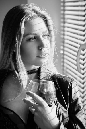 girl in lingerie with wineglass looking at window, monochrome imageの写真素材