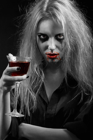 blond witch with bloody glass on black backgroundの写真素材