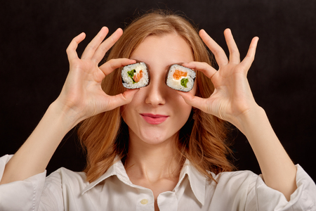 happy young woman playing with sushi on black backgroundの写真素材