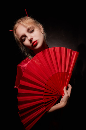 girl in geisha costume with red fan on black backgroundの写真素材