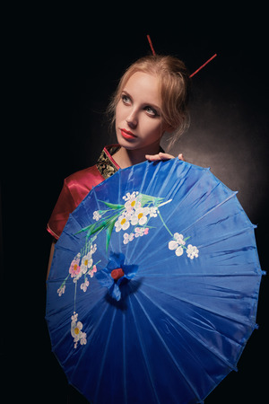 beautiful girl in geisha red costume with umbrella on black background, toned imageの写真素材