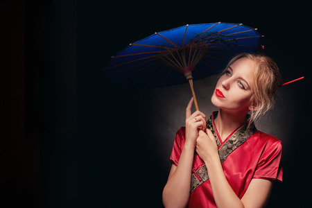 beautiful girl in japanese red costume with umbrella on black background, toned imageの写真素材