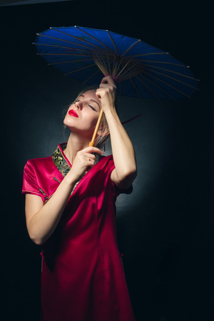 beautiful girl in japanese red dress with umbrella on black background, toned imageの写真素材