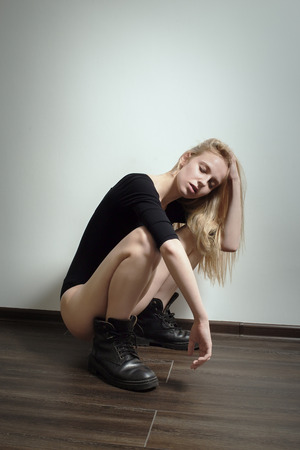 sad blond girl in black male boots sitting squat on floorの写真素材