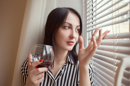 sad woman with wineglass looking at windowの写真素材