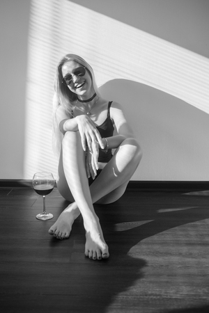happy blond girl with wineglass sitting in sunlight on floor, monochromeの写真素材