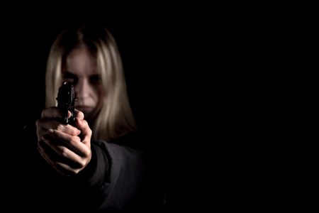 serious girl with gun aiming on black background with copyspaceの写真素材