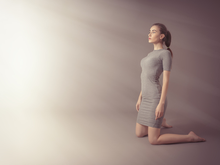 serious girl on knees in sun light rays at gray backgroundの写真素材