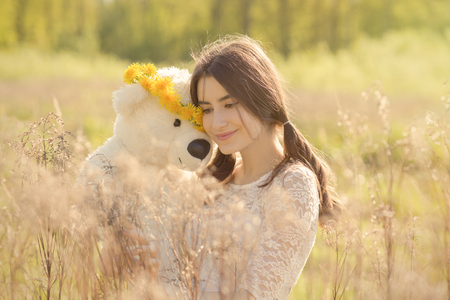 happy girl with teddy bear in dry grass, toned imageの写真素材
