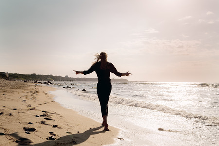 sad blond barefoot woman walking away at sunny sea beach, toned imageの写真素材