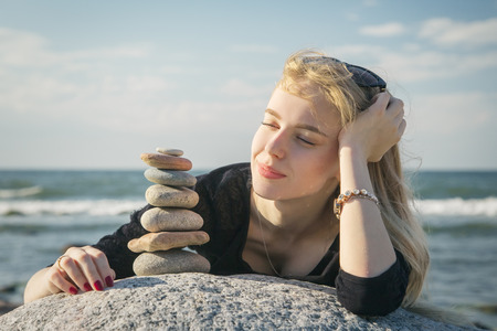 beautiful woman stacking stones on rock at sunny sea beachの写真素材