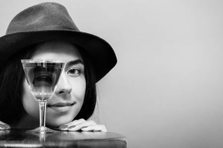 fun girl looks at camera through wineglass on gray background, monochromeの写真素材