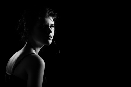 beautiful sad young woman on black background with copy space looking at camera, monochromeの写真素材