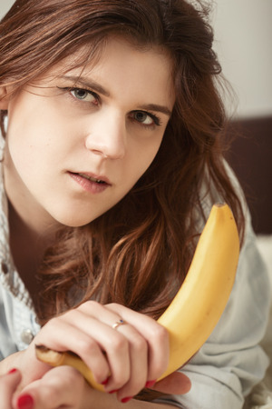 sensual sad young woman with banana lying on bedの写真素材