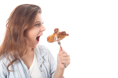 fun young woman eats fried chicken thigh on white background with copy space isolatedの写真素材