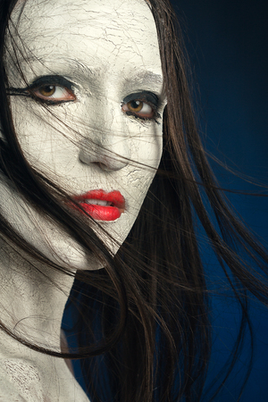 girl with white cracked make-up on blue backgroundの写真素材