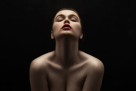 beautiful young naked woman posing sensually holding head up on black backgroundの写真素材