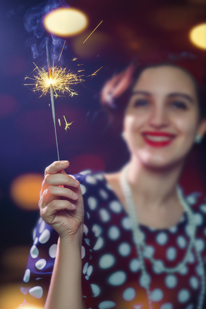 blurred woman with burning sparkler on dark background with lightsの写真素材