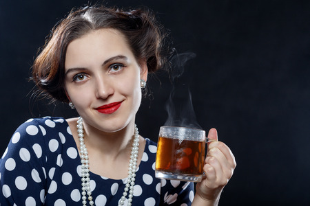 beautiful pinup woman with cup of tea on black background looking at camera smiling