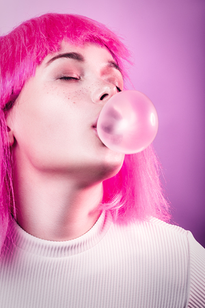 girl in a wig inflates a bubble from chewing gum toned imageの写真素材