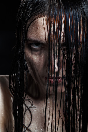 serious angry woman with wet black hair looking at cameraの写真素材