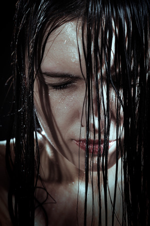 serious sad woman with wet black hair close her eyes in darkの写真素材