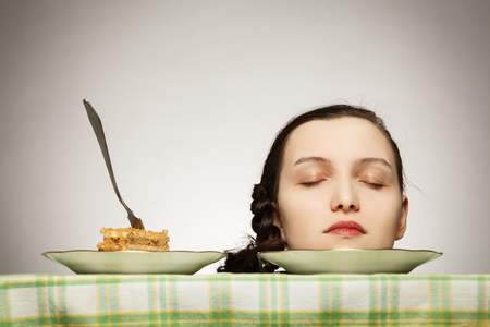 female head with closed eyes lying in dish near sweet pie on a tableの写真素材