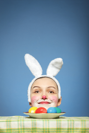 easter rabbit head with multicolored eggs lying on dish at blue backgroundの写真素材