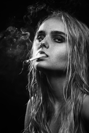 serious young blond woman on dark blue background smoking, monochromeの写真素材