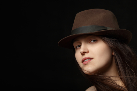 woman with hat and blowing hair on black background with copy space looking at cameraの写真素材