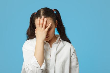 Beautiful young woman with headache touching her forehead on blue backgroundの写真素材