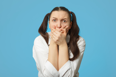 shocked girl on blue background cover her mouthの写真素材