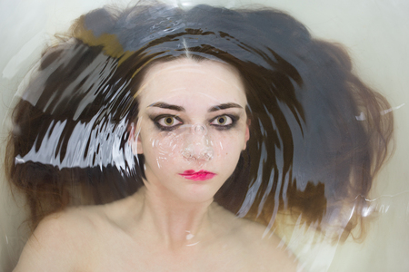 beautiful woman soaks in the warm water and looking at camera, closeup portraitの写真素材