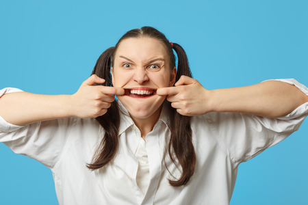 fun woman grimacing shows her teeth on blue backgroundの写真素材