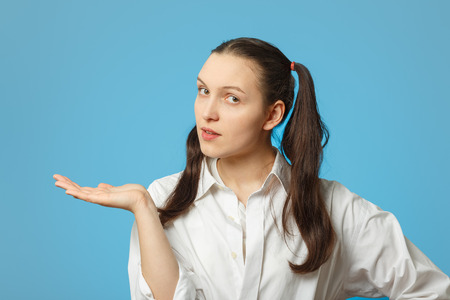 serious girl on blue background show open palm with place for productの写真素材