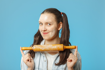 happy woman with a rolling pin is soiled in flour on blue background smilingの写真素材