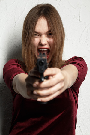 fun girl with gun on white background aiming at camera, screamingの写真素材