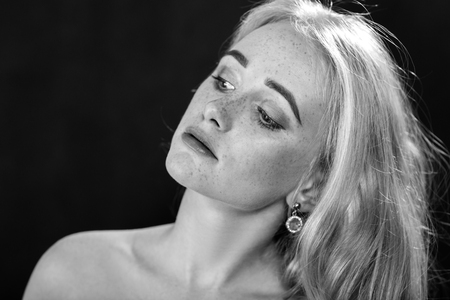 sad girl with freckles and bare shoulders on black background, monochromeの写真素材