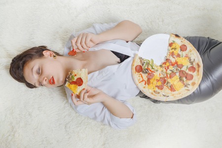beautiful overeat businesswoman lying with pizza piecesの写真素材