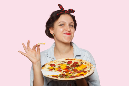 happy woman with pizza on pink background eats, looking at cameraの写真素材