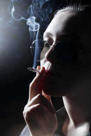 serious woman smoking cigarette on black background, profile viewの写真素材