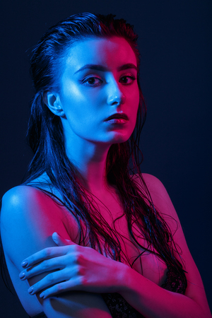 serious young woman in multicolor lights on black background looking at cameraの写真素材