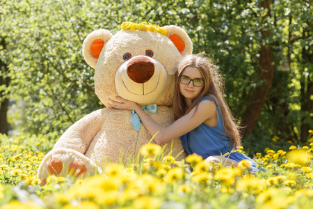 girl with teddy bear sitting on dandelion meadowの写真素材