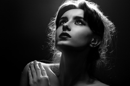 sad young woman in back lights on black background looking up, monochromeの写真素材