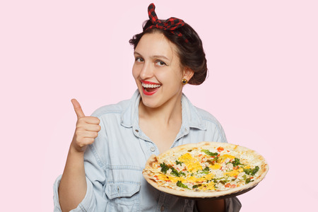 happy woman presents pizza on pink backgroundの写真素材