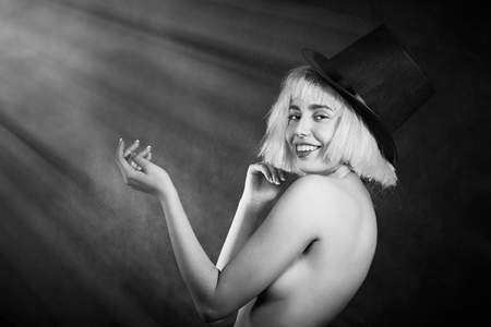 slim happy topless woman in wig and hat on black background with light rays smiling, monochromeの写真素材