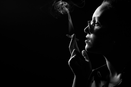serious woman smoking cigarette on black background, profile view, monochromeの写真素材