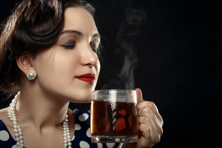 beautiful pinup woman with cup of tea on black background with copy space smell smilingの写真素材